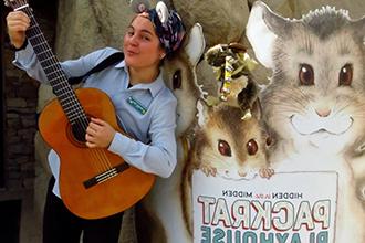 Educator Michelle plays guitar next to the entrance to Packrat Playhouse