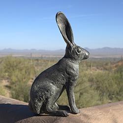 长耳兔青铜雕塑坐落在土坯墙上，以沙漠景观和蓝天为背景